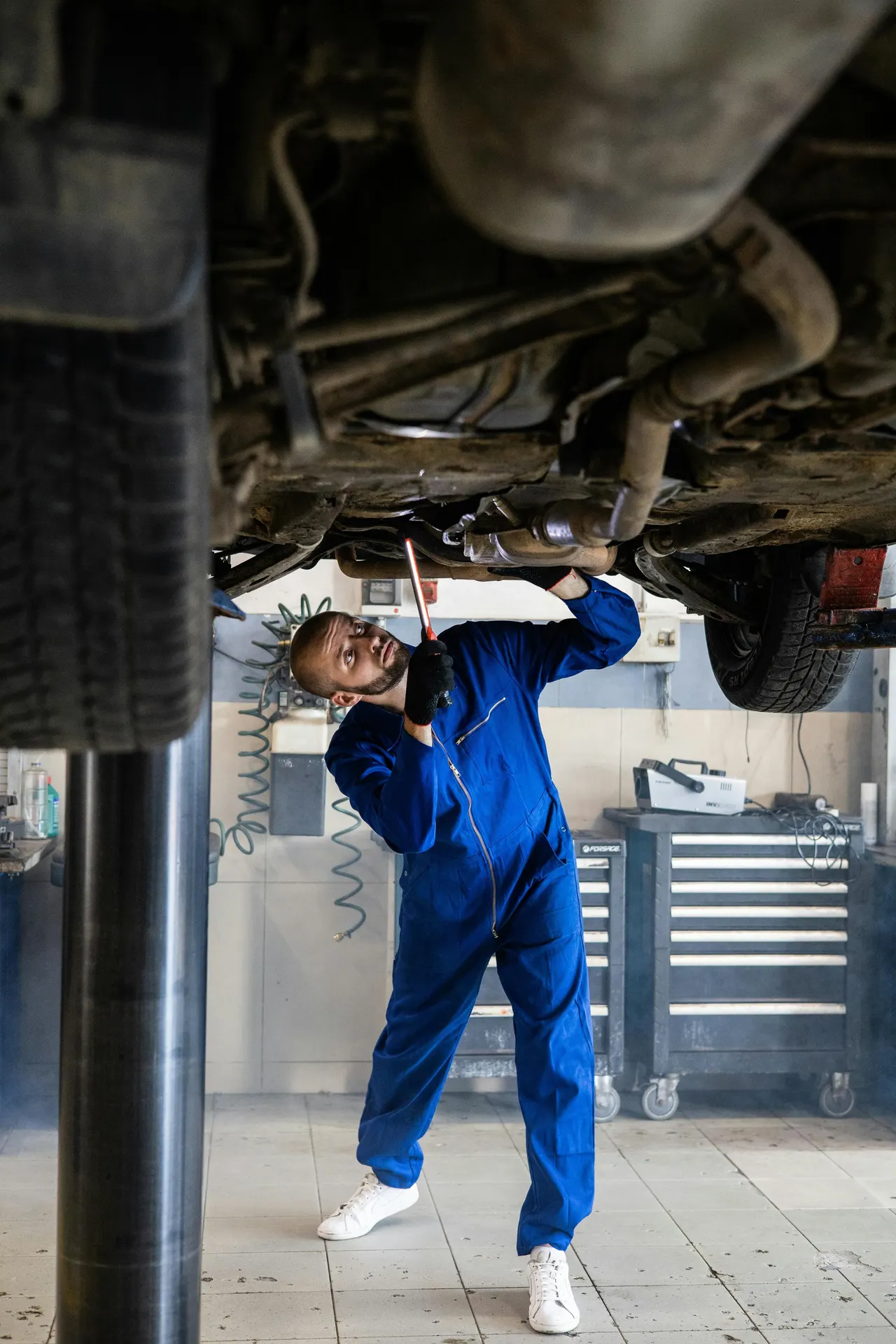 Techniker bei der Arbeit unter einem Fahrzeug auf der Hebebühne einer Werkstatt